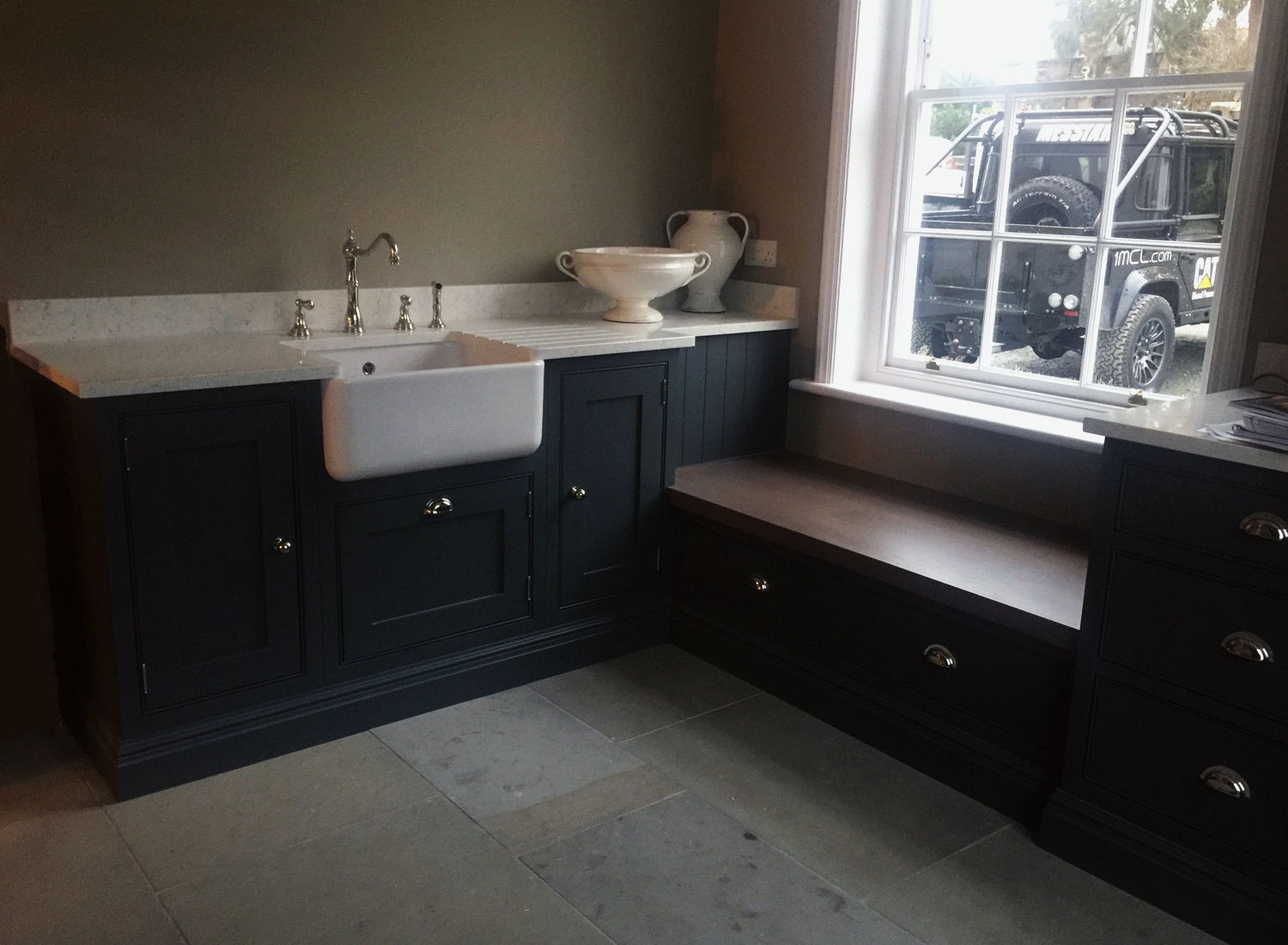 A boot room with a painted bench seat and a butler sink under the window