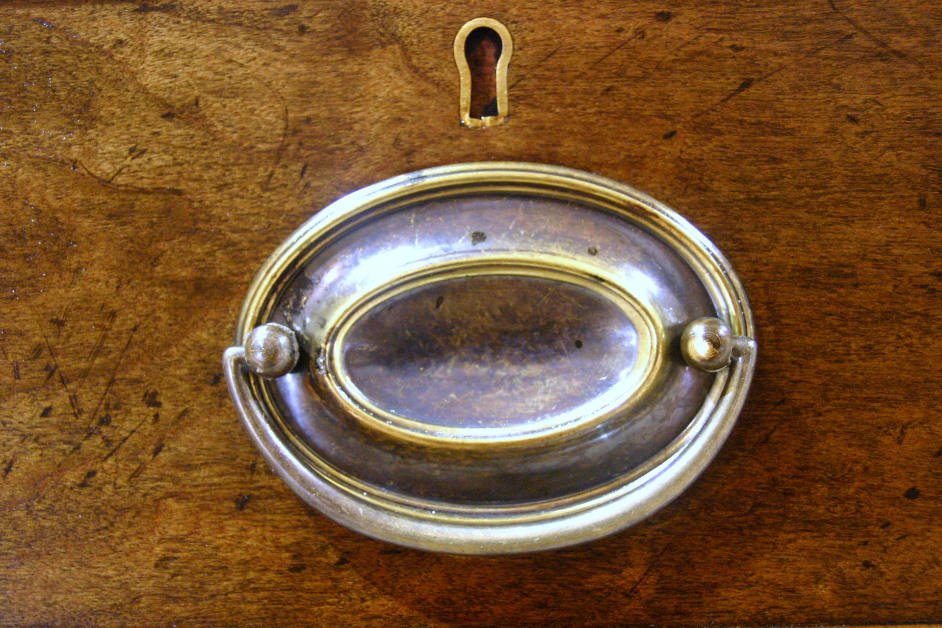 An aged brass drawer handle and escutcheon set into figured cherry on a tea caddy chest