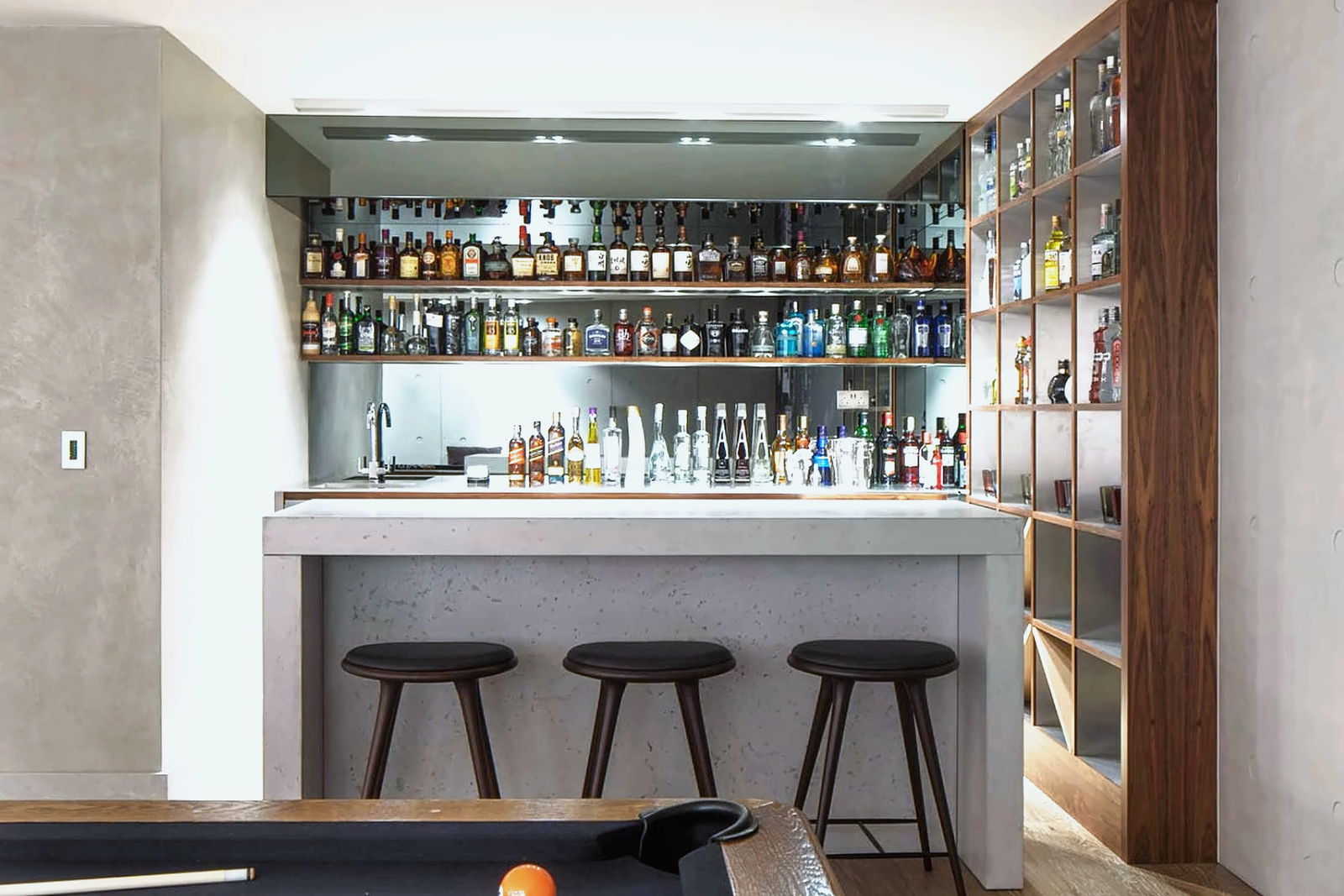A residential bar and drinks room with illuminated bottle shelving and a pool table